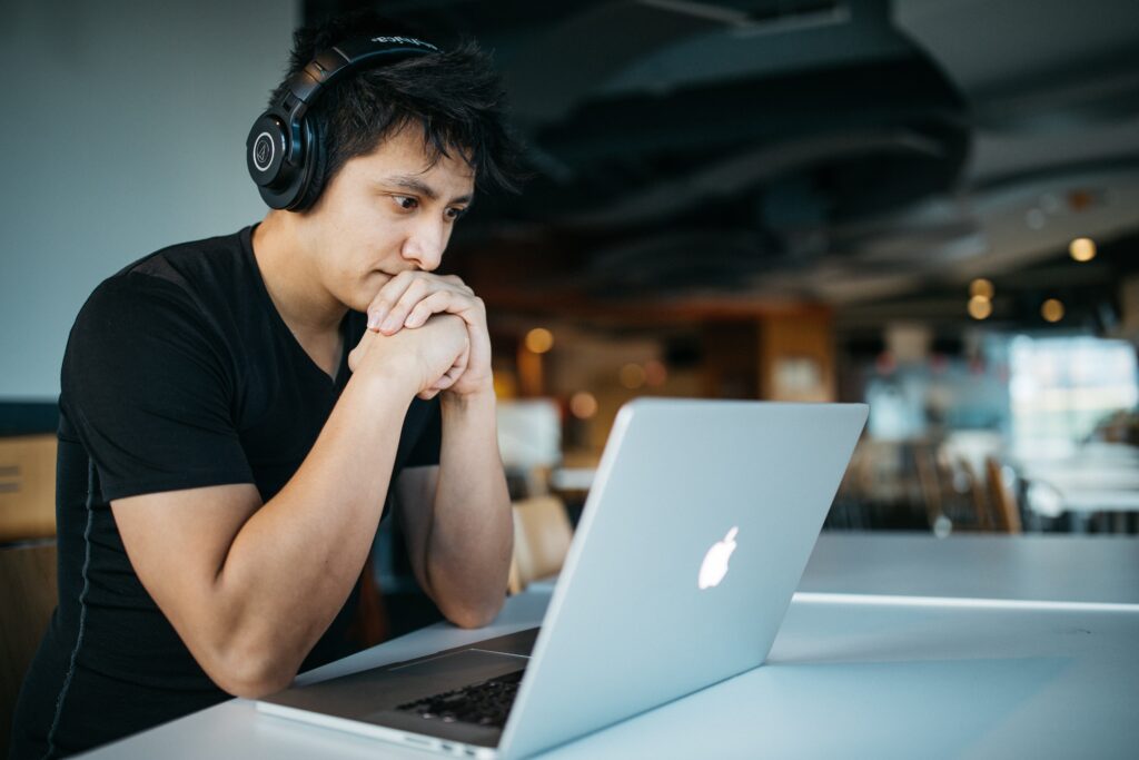Man wearing headphones while sitting on a chair in front of his macbook as if in a meeting over Zoom.